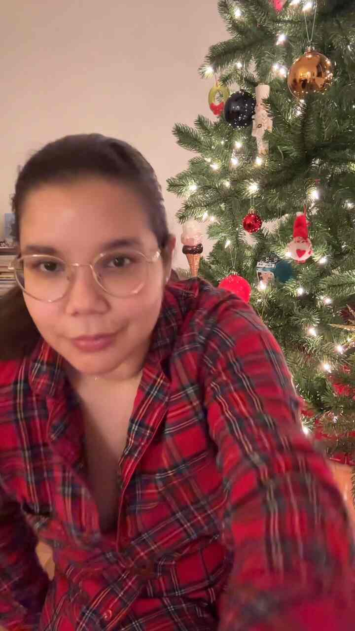 Cozy modern living room with a decorated Christmas tree and a person wearing a red plaid shirt under warm lighting