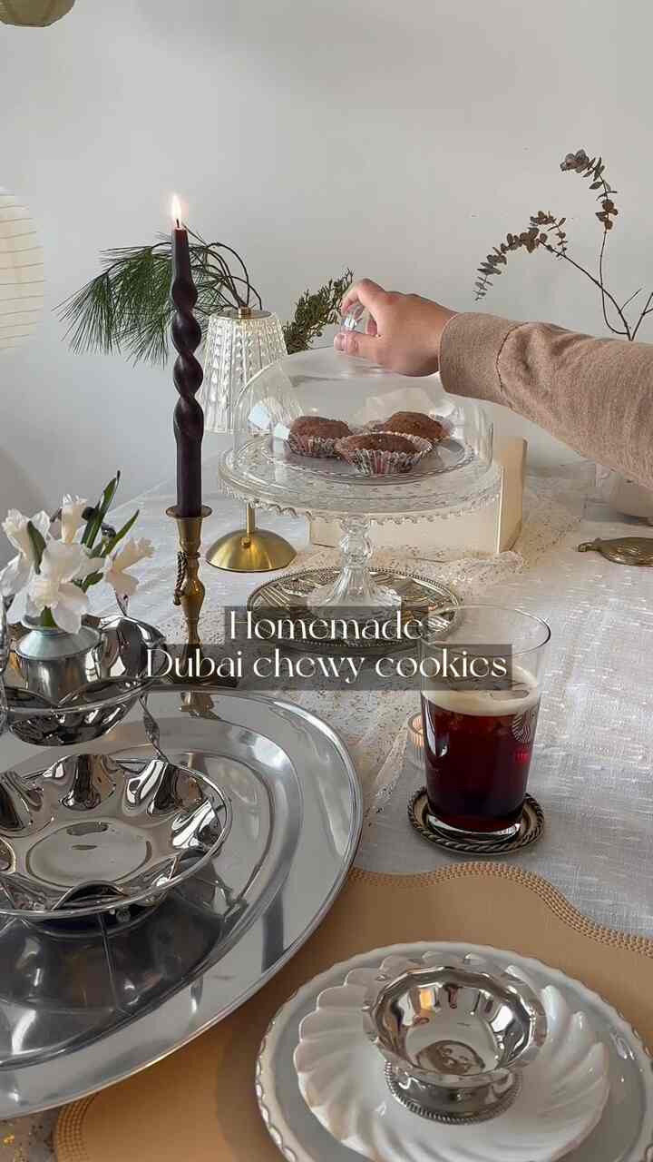 Transparent glass cake stand, gold accents, and candle arranged on white table in a cozy home cafe setting