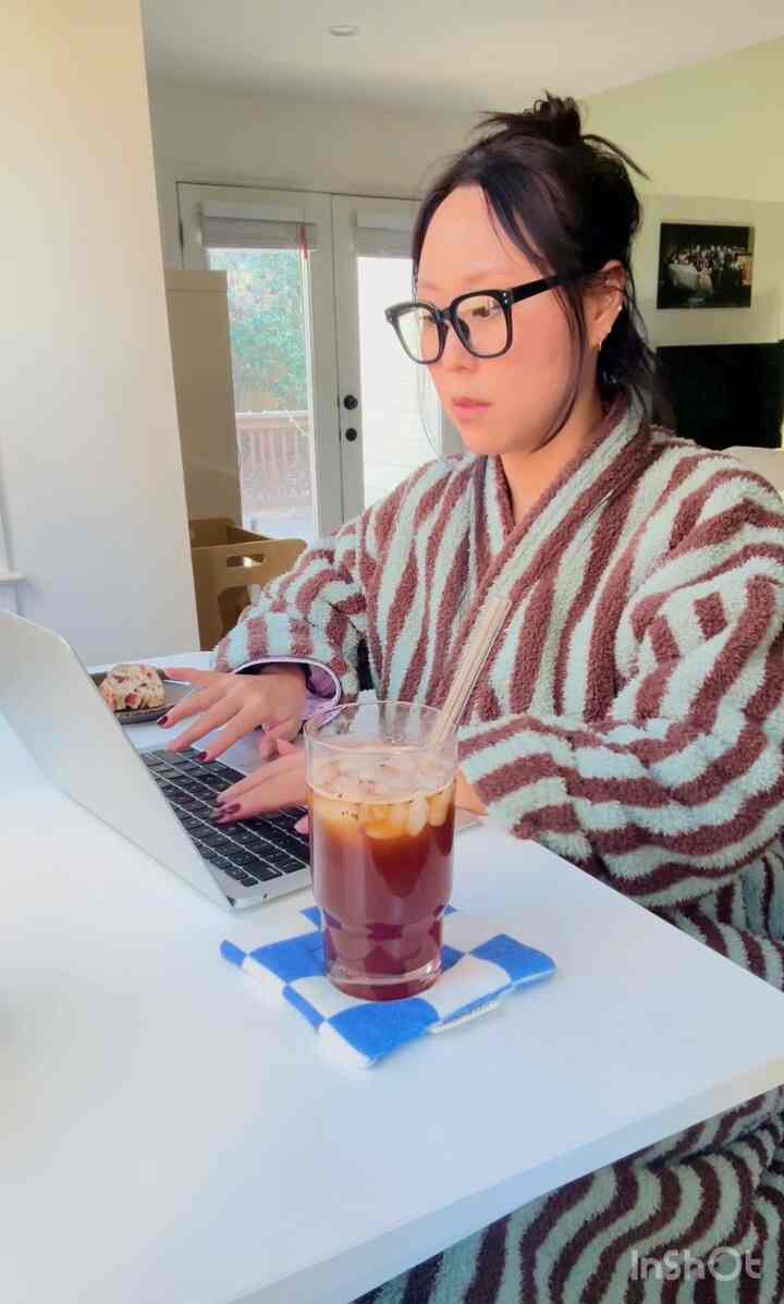 White and brown toned home office space featuring a person working on laptop with iced coffee, exuding a cozy remote work atmosphere