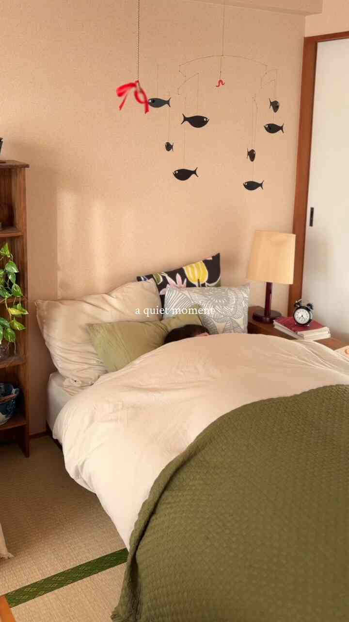 ベージュ色調の畳の寝室にスライディングドアと魚のモビール、木製の本棚、オリーブグリーンの寝具が配置された雰囲気のあるインテリア