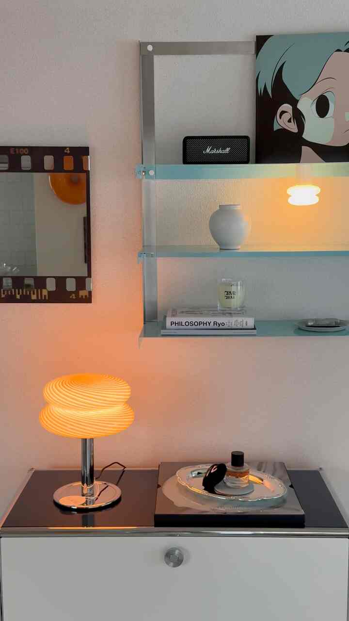 明るい白い壁とサイドボードの空間、オレンジ色のテーブルランプと透き通った青い棚が配置されたモダンで温かみのあるインテリア