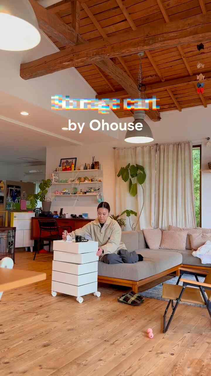 木目調の床と天井が特徴的なミッドセンチュリーモダンのリビング、キャスター付きの白いキャビネットと快適なソファが配置された暖かみのある印象的な空間