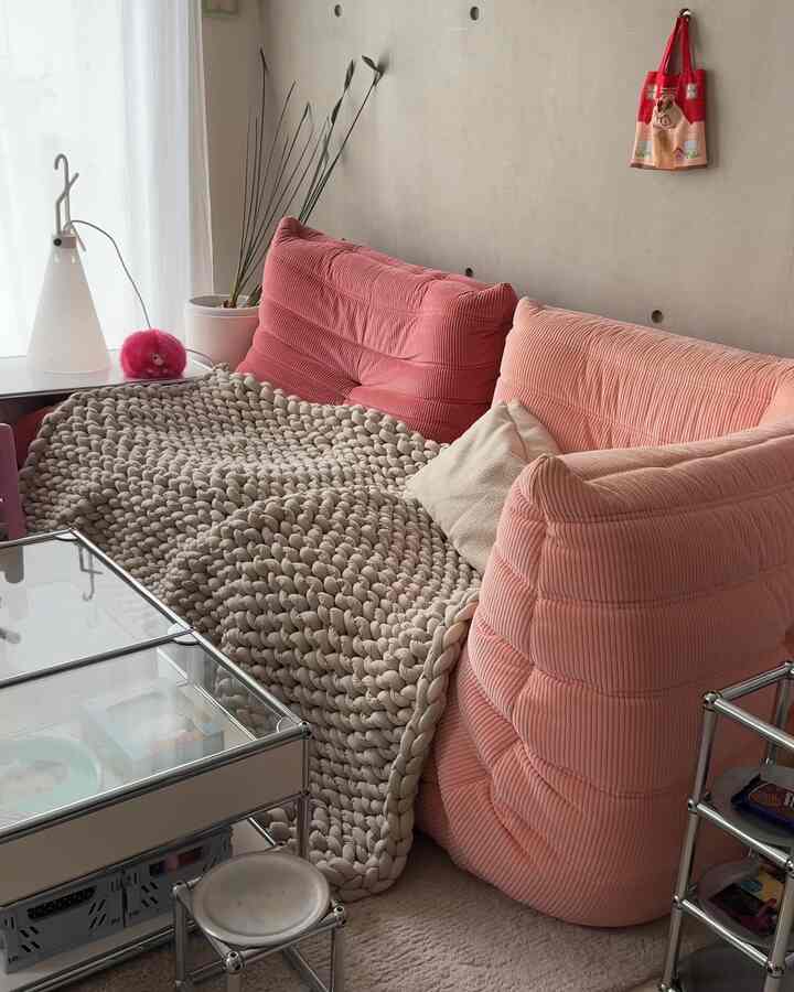 ナチュラルな雰囲気のリビング、ピンクのソファとベージュのブランケットが配置され、柔らかな自然光が差し込む空間