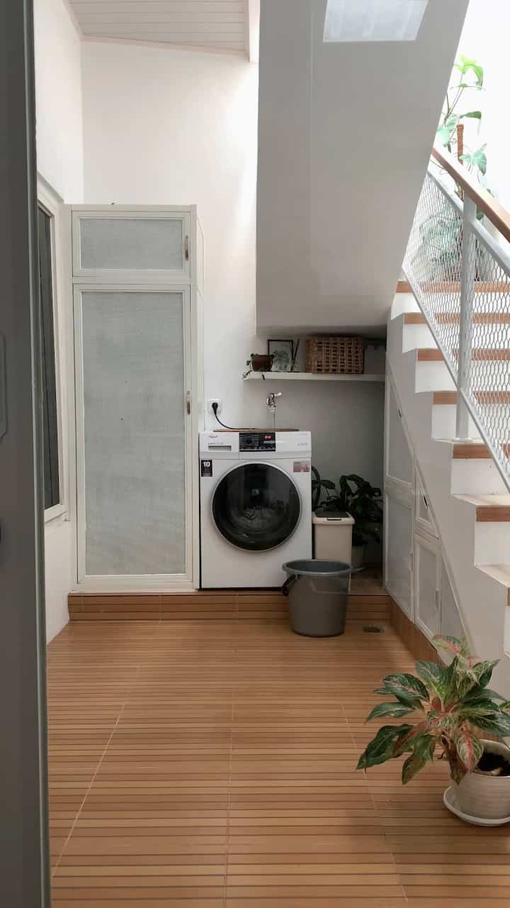 White and wood-toned narrow laundry room under stairs, featuring washing machine and storage cabinet with a clean atmosphere