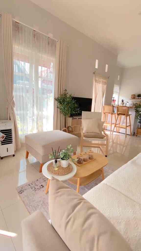 Bright natural-tone living and kitchen area featuring large windows with floor-length curtains, minimal and cozy interior design