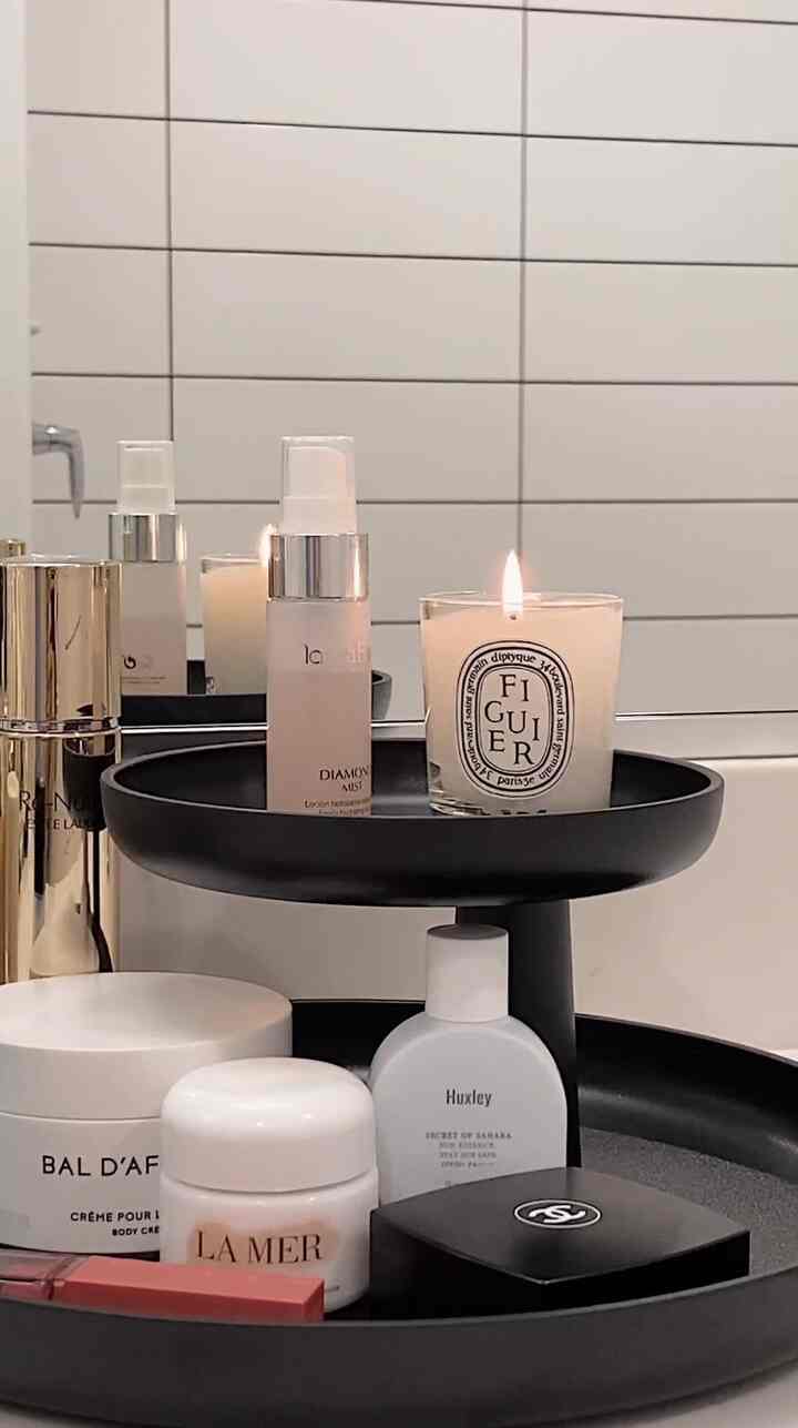 Modern bathroom space with white tiled background featuring a black Vitra tray holding candle and skincare products