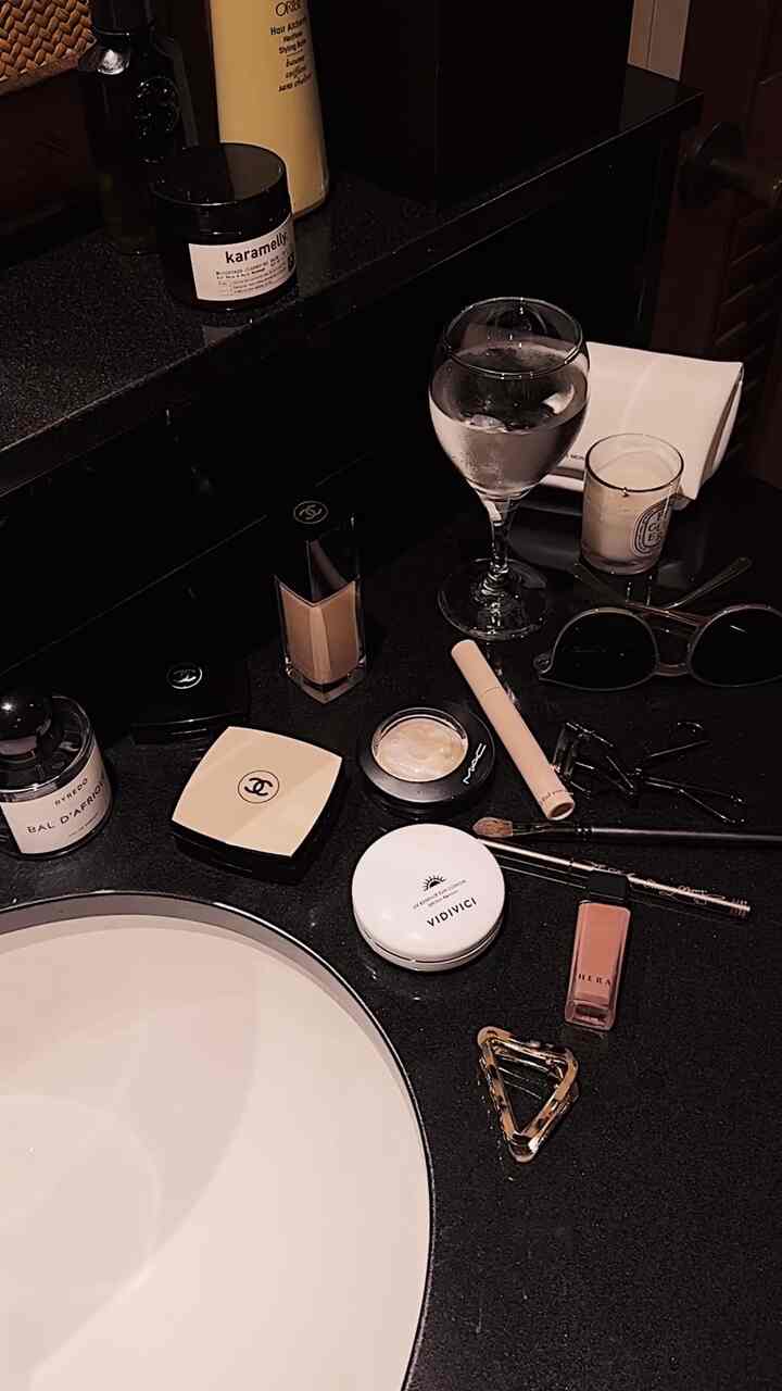 Black-toned bathroom vanity featuring makeup products, a wine glass, and a candle creating a chic atmosphere