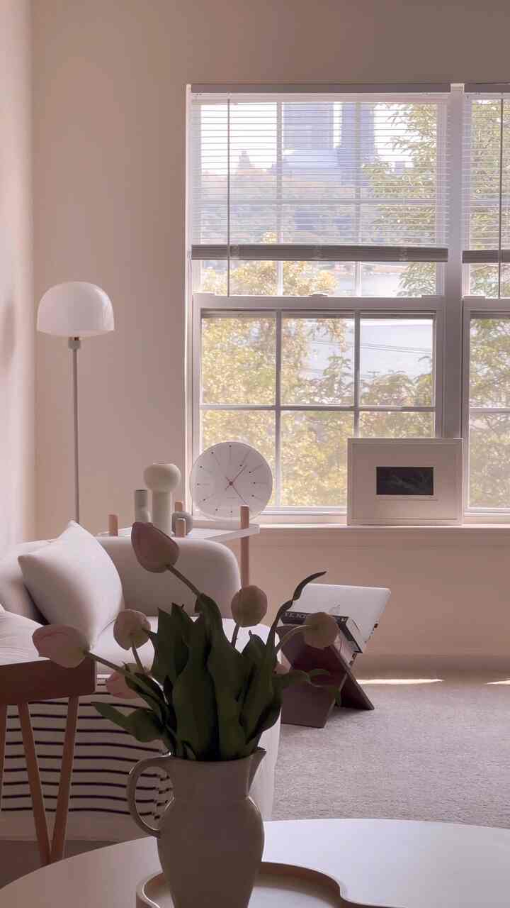 Beige-toned living room with white sofa, wooden chair, and coffee table featuring vase of flowers in cozy atmosphere