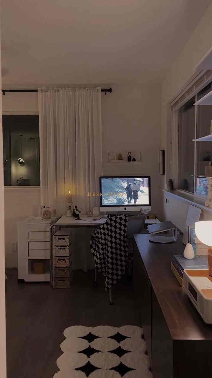 Monotone home office space featuring a white desk with computer center, dark brown console and floor, white curtains, and a patterned rug creating cozy ambiance