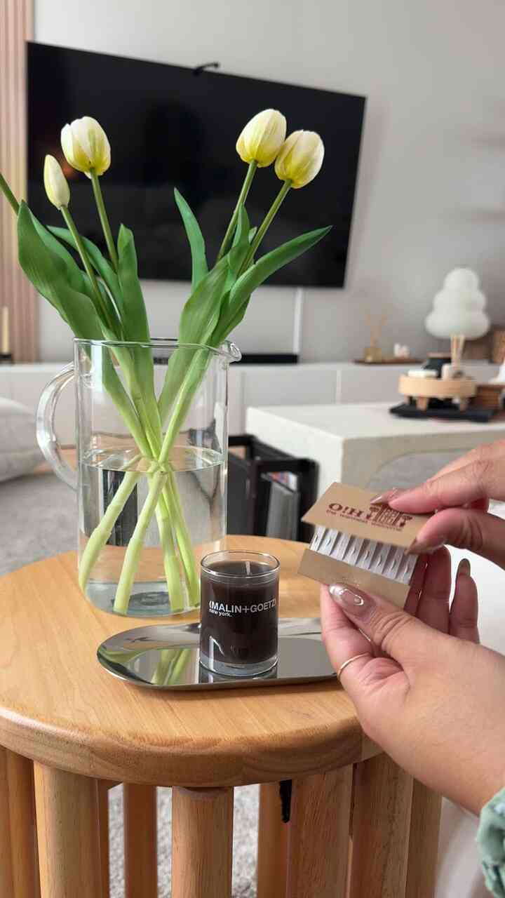Cozy living space featuring natural wood tone round table with transparent vase holding white tulips and a small black candle