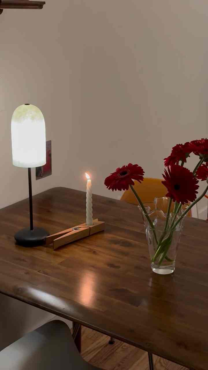 Brown wood-tone dining room featuring red flowers, a lit candle, and warm table lamp, creating a simple and natural atmosphere