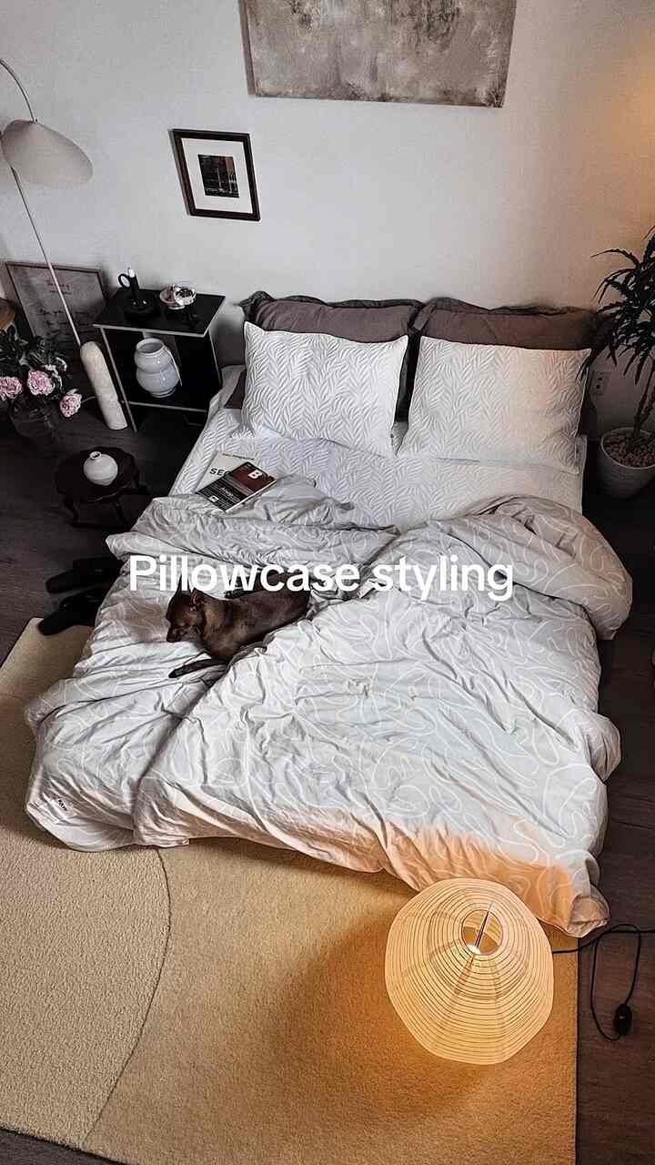 Natural-toned bedroom featuring a large bed with pillows, rug, floor lamp, and plant creating a cozy atmosphere