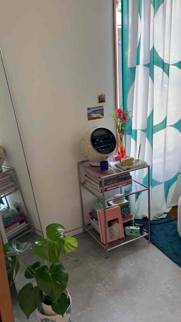 白い壁と緑の柄カーテンがある1LDKリビングコーナー、クロームのサイドテーブルと観葉植物が配置されたミッドセンチュリーモダンな印象的な空間