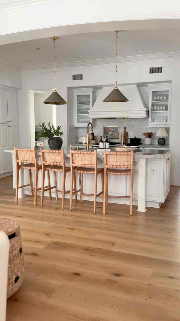 Modern kitchen featuring white cabinetry, four woven stools, and warm wood-tone flooring with a clean atmosphere