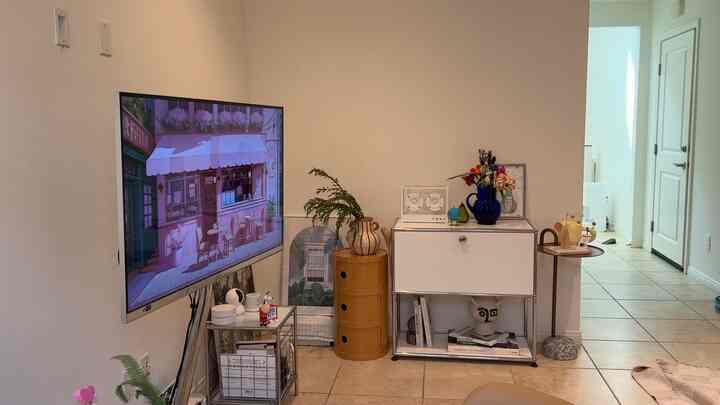Mid-Century Modern living room with white walls and beige tiled floor, featuring a TV and colorful decor in a cozy setting