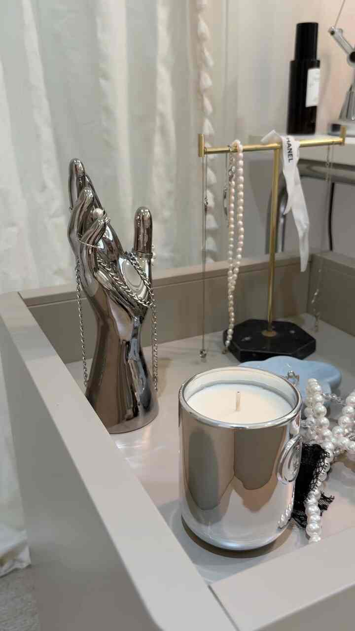 A cozy interior decor space featuring silver-toned candle, decorative hand sculpture, and pearl necklaces