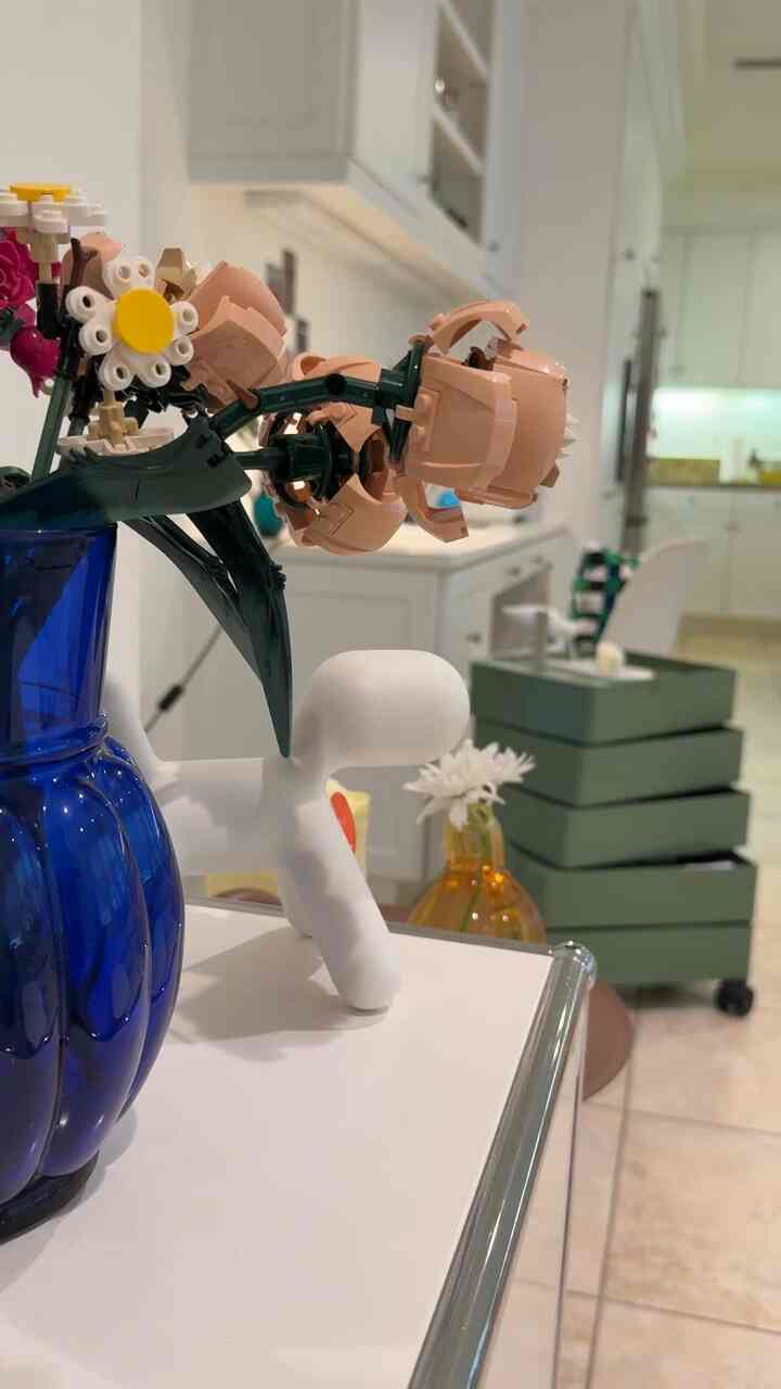 A white and blue-toned kitchen space featuring vases and a pet-inspired sculpture in a clean mid-century modern style interior