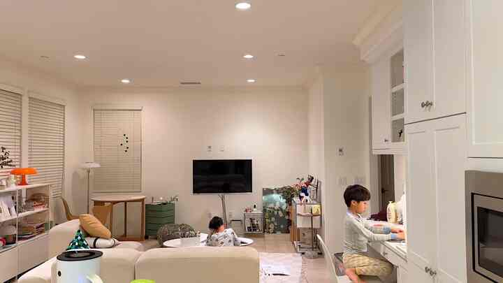 Bright family living space with white and beige tones connecting living room and kitchen, featuring two children actively present