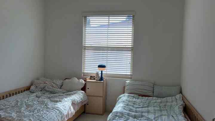A natural-toned kids' room with white walls and window, featuring two children's beds and a cream dresser creating a cozy atmosphere