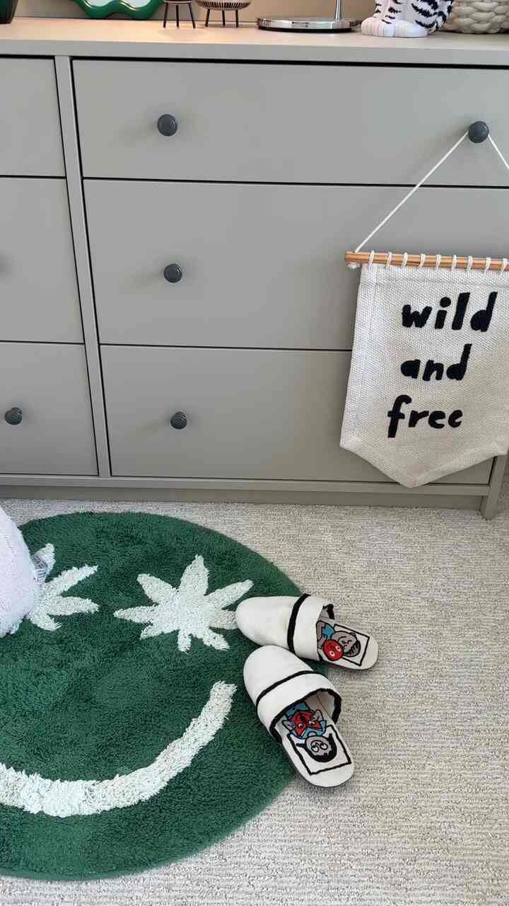 Minimal kids' room featuring a gray dresser, green rug, and children's slippers arranged neatly