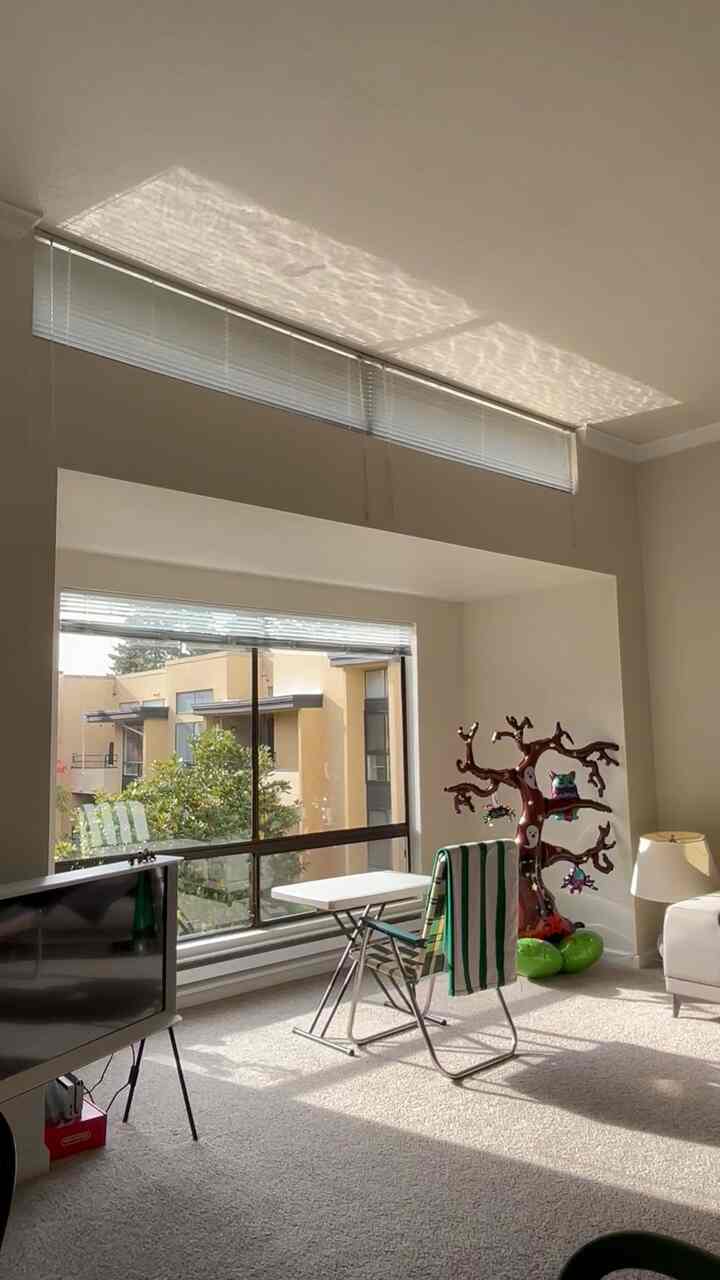 Bright beige-toned living room with large window, featuring white sofa and folding table and chair in a clean, open layout