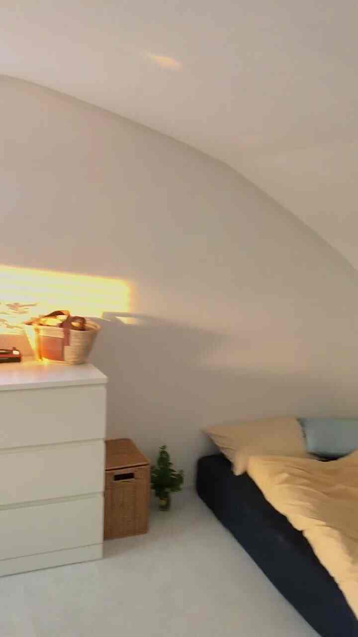 Warm sunset light reflects on white-toned bedroom featuring a navy bed with yellow duvet, creating cozy atmosphere