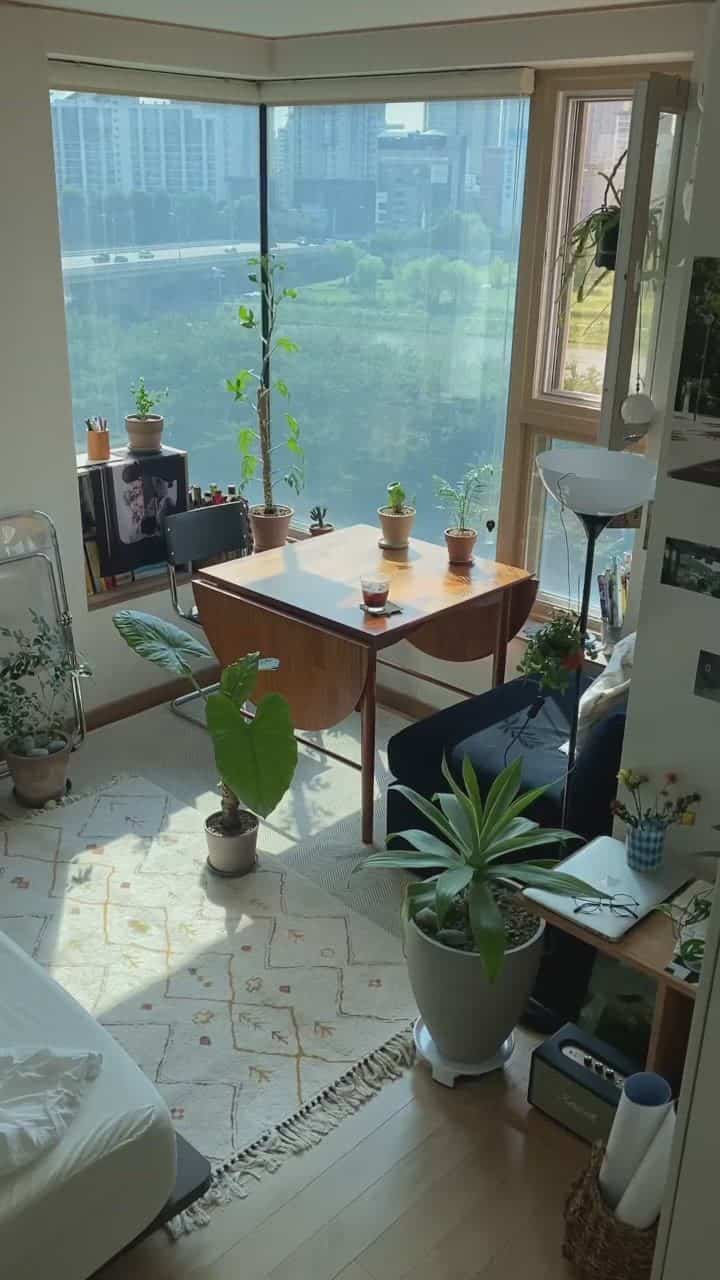 Bright white walls and wood-tone flooring in a Nordic-style studio living room featuring a wooden table and abundant indoor plants