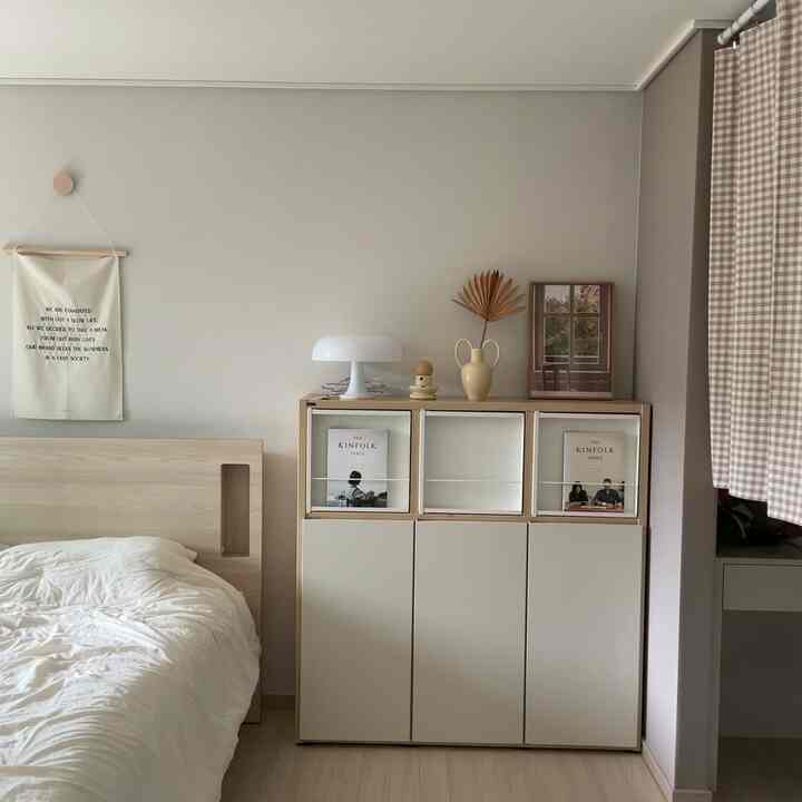 ベージュと木目調が調和したシンプルな寝室、木製ベッドとキャビネットが自然な雰囲気を演出している