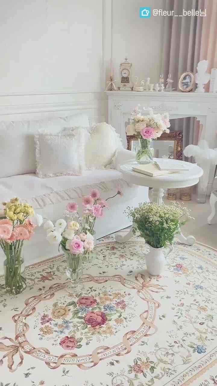Soft white-toned living room featuring a floral patterned rug, white sofa, flower vases, and intricate decorative elements creating a romantic atmosphere