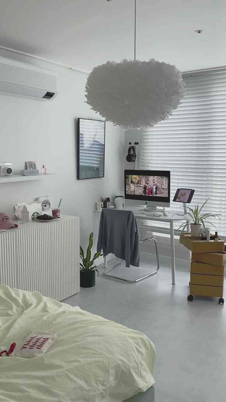 A white-toned bedroom and home office featuring a desk, chair, dresser, yellow trolley, and plant in a minimal modern style