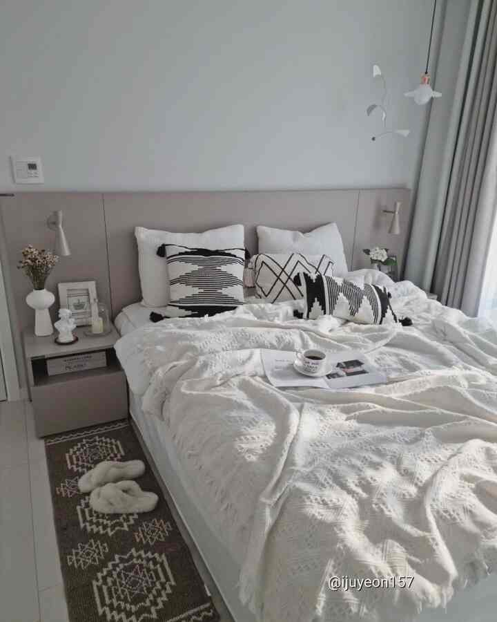 A white and beige toned bedroom featuring cozy bedding and black-and-white patterned cushions creating a calm atmosphere