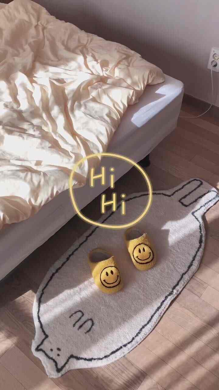 白とベージュのトーンの子供部屋、寝具と猫の形のラグ、黄色のスマイルスリッパが配置された印象的な空間