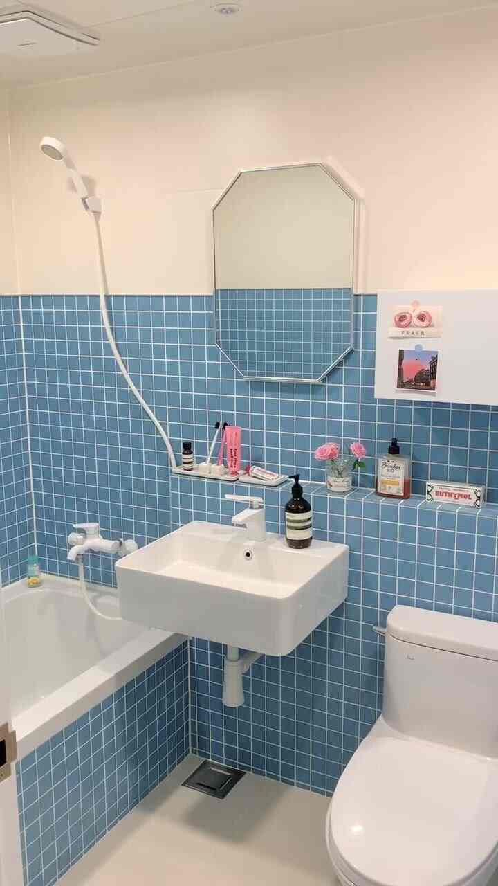 明るい青いタイルと白い設備が配されたコンパクトなバスルーム、ヴィンテージな小物とピンクのバラが調和した清潔感のあるインテリア