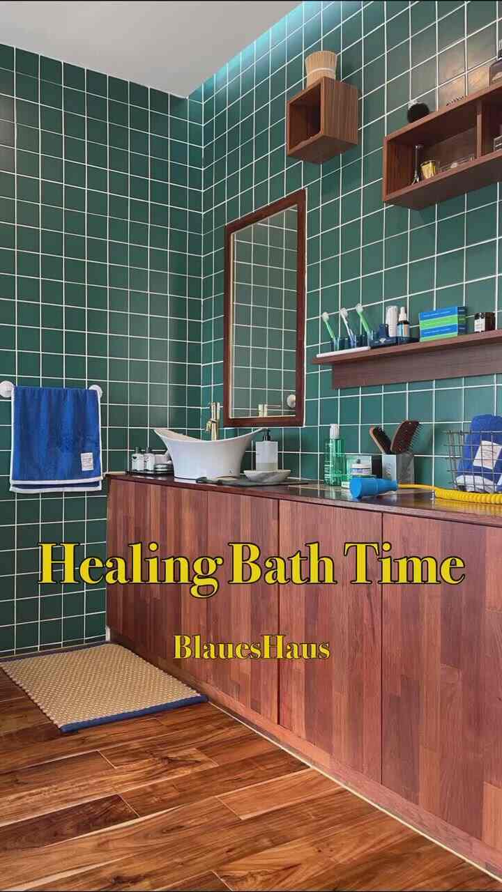 Green tiled walled bathroom featuring wooden cabinetry and blue towels with a warm, vintage atmosphere