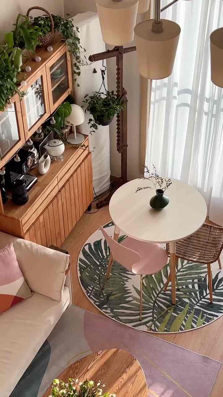 Natural wood-toned living room featuring wooden cabinet, round table, fabric sofa, and abundant plants creating a cozy atmosphere