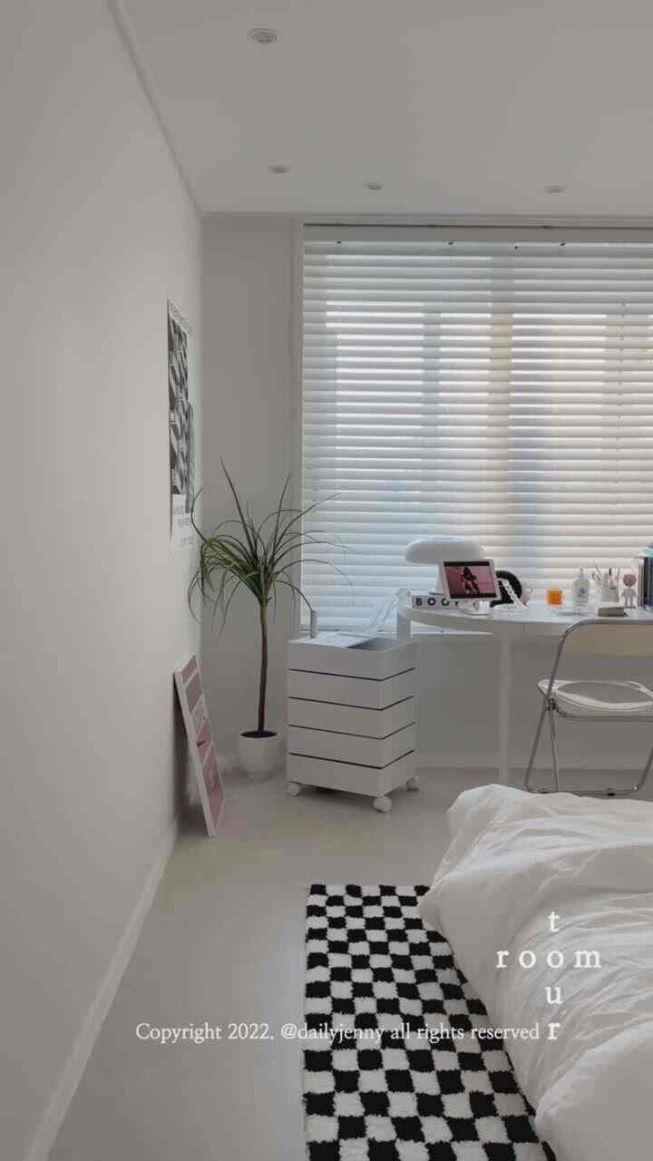 White-toned bedroom featuring a desk and rolling drawer by the window, showcasing a simple and cozy atmosphere