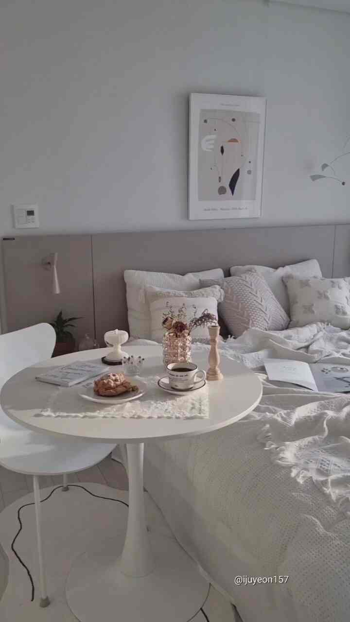 Soft white-toned bedroom featuring a white bed and round table with coffee and bread, creating a cozy atmosphere