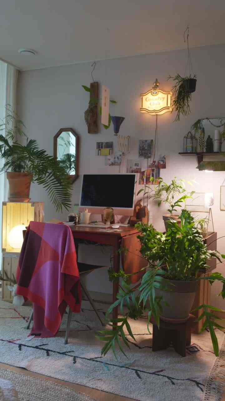 Natural-toned study featuring a central desk with numerous plants, creating a cozy workspace
