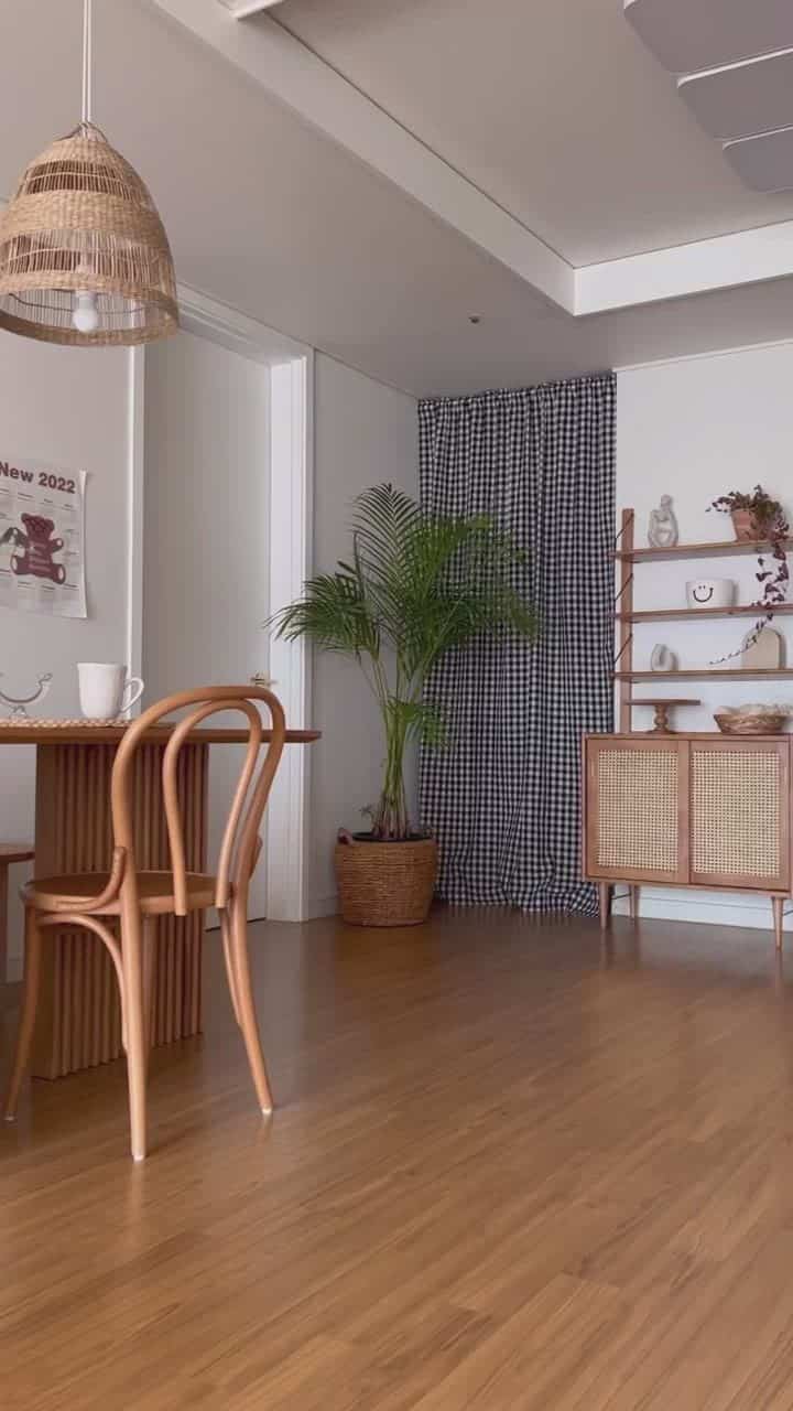 Natural-toned living room featuring a wooden dining table, rattan pendant lamp, and checkered fabric poster in a simple interior