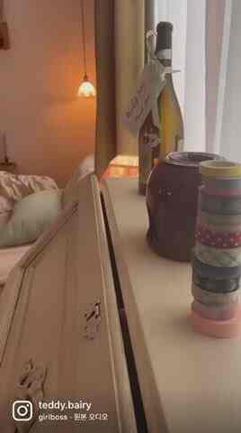 Studio bedroom dominated by olive green curtains, featuring a bed, nightstand, vintage lighting, and rug creating a cozy atmosphere