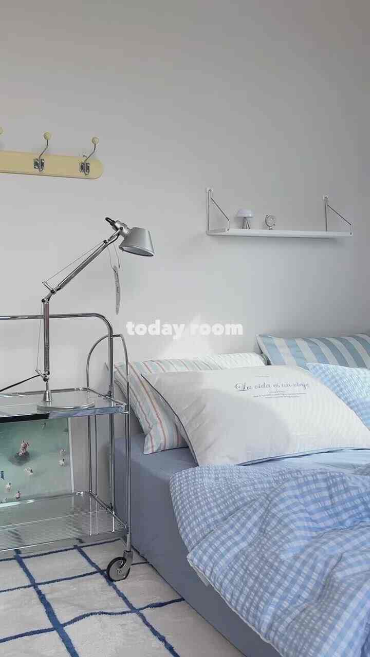 Soft blue and white toned bedroom featuring checkered rug, metal side table, and adjustable lamp in a simple, cozy space