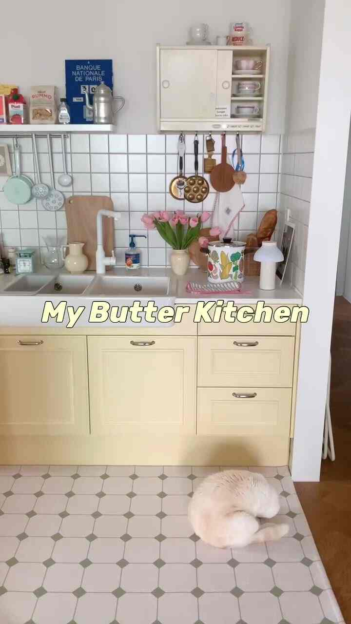 黄色の下部キャビネットと白いタイル壁が調和した整然としたキッチン、中央にピンクのチューリップが飾られ、猫が眠っている