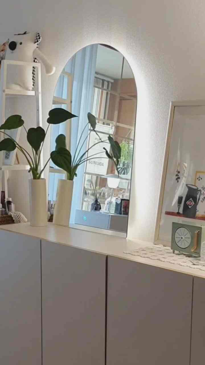 White and natural toned living room space featuring an arch-shaped backlit mirror and plants with a modern clean design