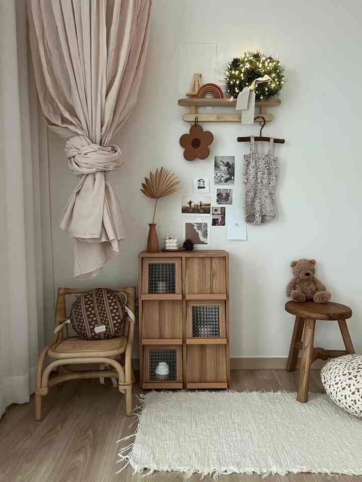 暖かみのあるウッドトーンとベージュカーテンが調和した、赤ちゃんの服やおもちゃが配置された雰囲気のある子供部屋