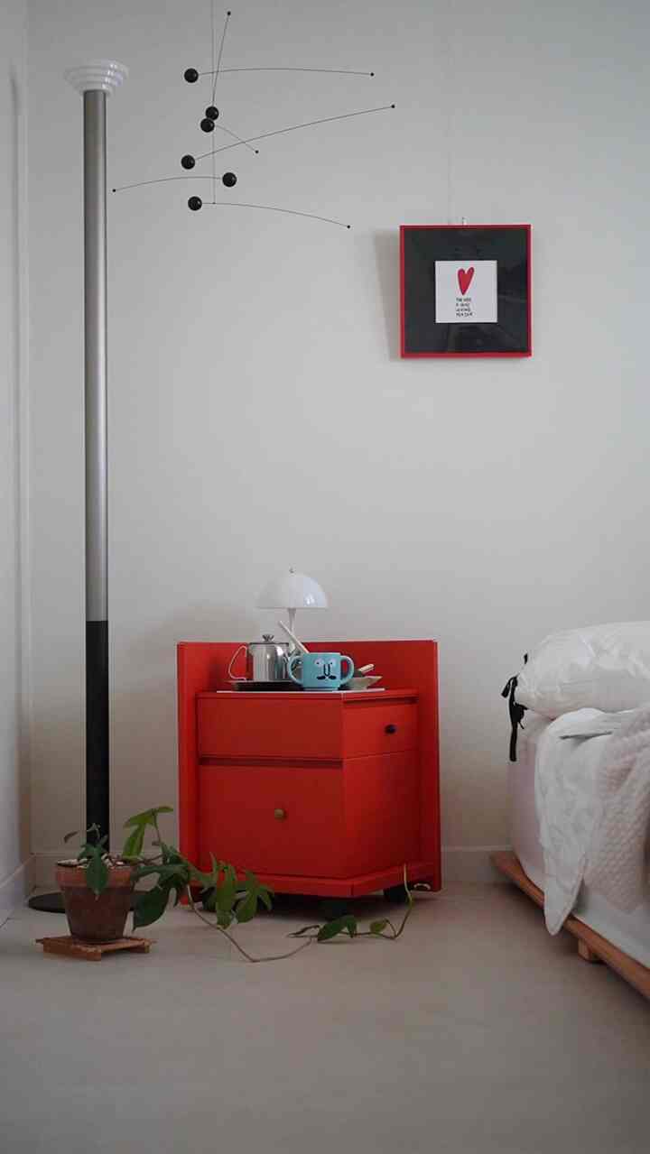 白い壁と寝具のある子供部屋、レッドのドレッサーとフレンステッドのモビールが配された印象的な空間