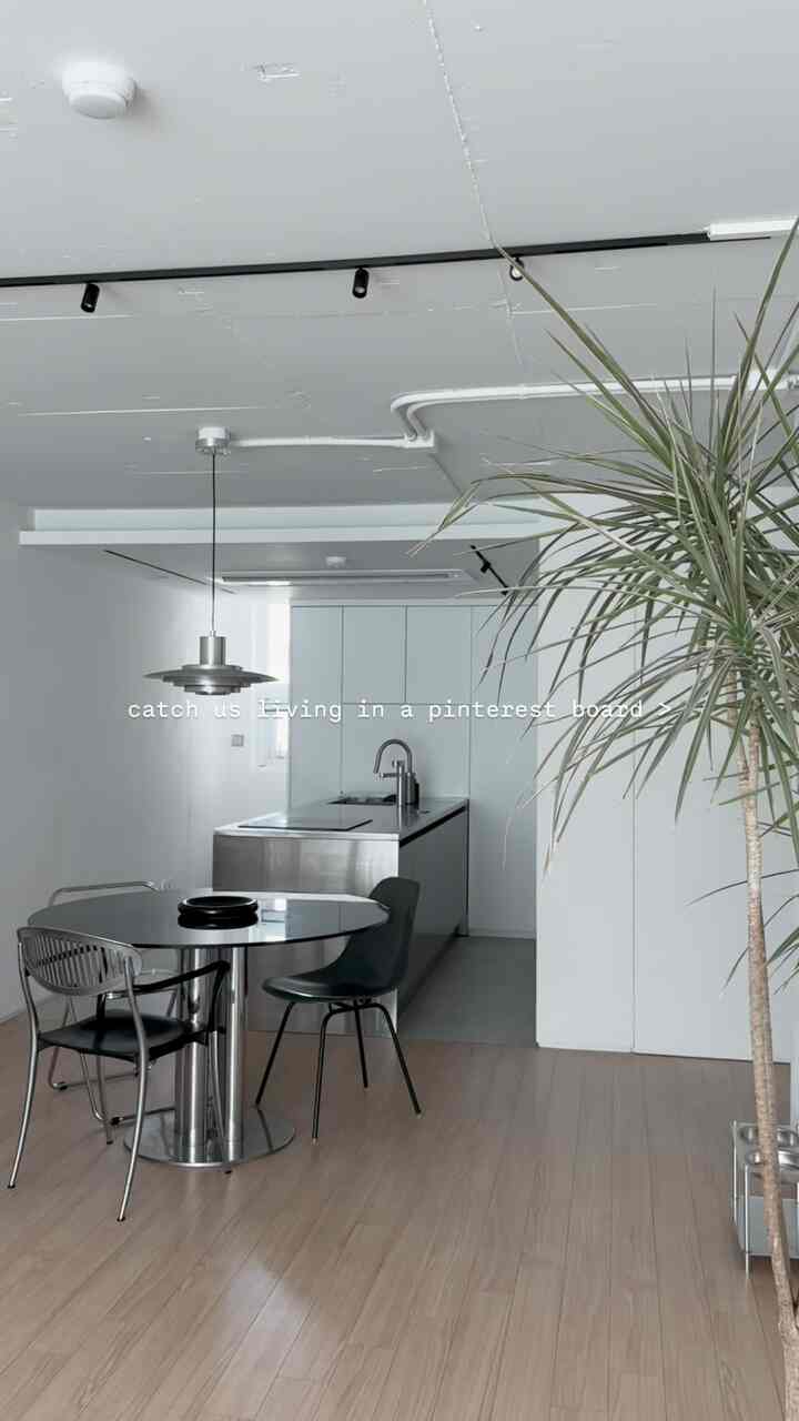 白い壁と天井、木目調の床が調和したモダンでミニマルなキッチンとダイニングスペース、ステンレスのテーブルと黒いダイニングチェアが配置されている空間