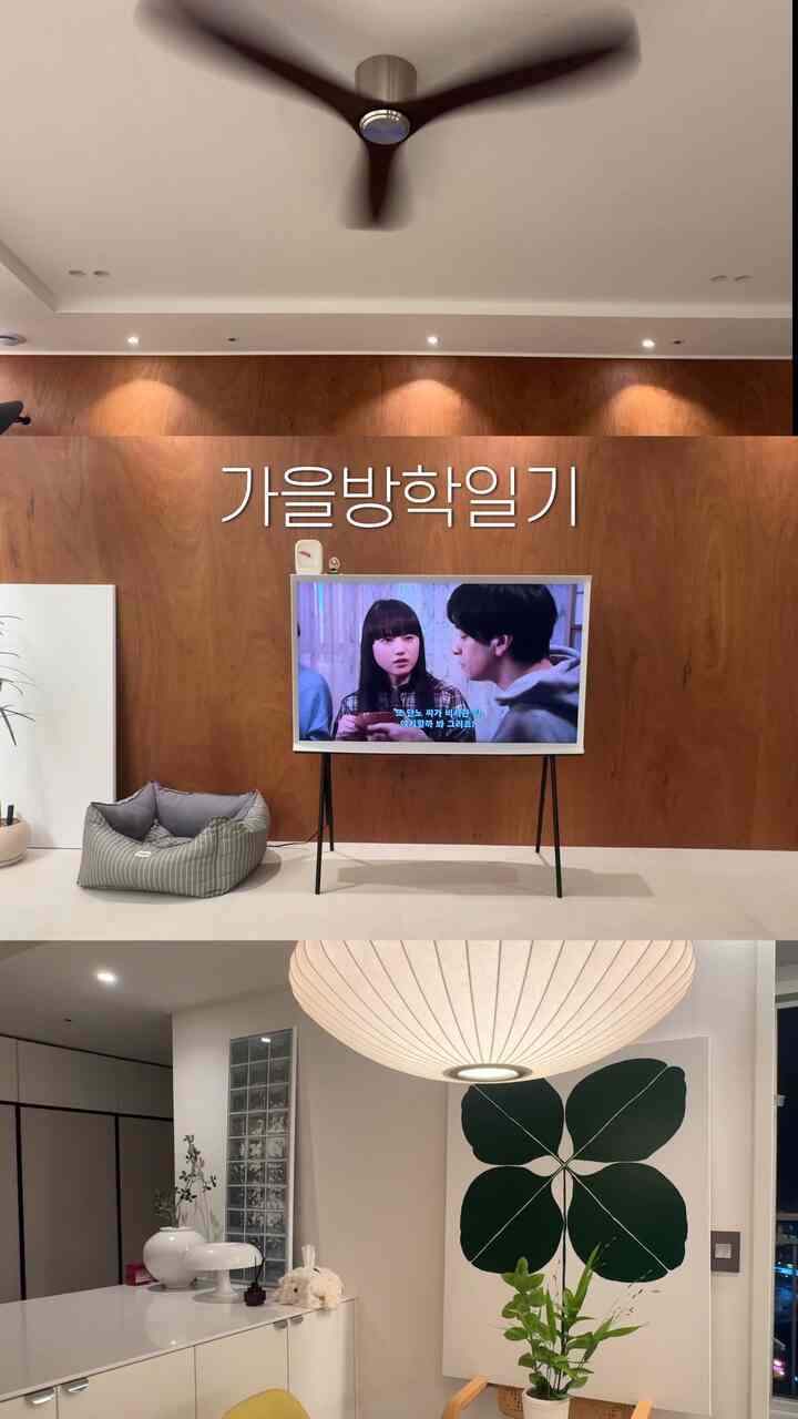 ホワイトとブラウンの色調のリビング、壁に大きなアートとテレビスタンド、植物やテーブルランプが配置されたナチュラルモダンなインテリア