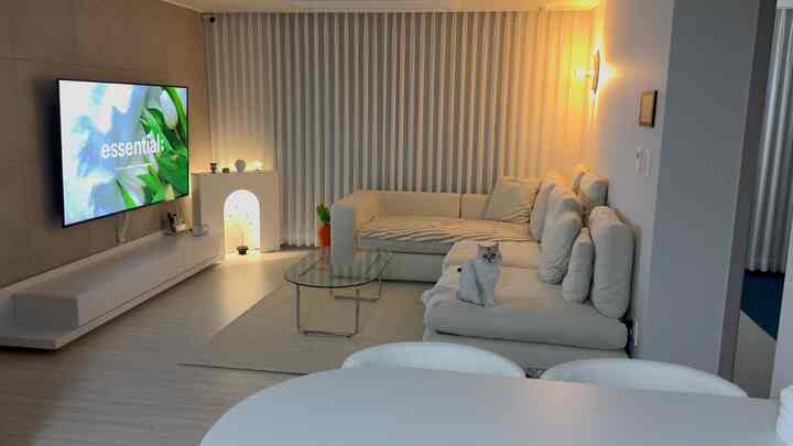 白とベージュの色調のリビング、広いソファとテレビコンソール、カーテンが配置された雰囲気のあるモダンな空間