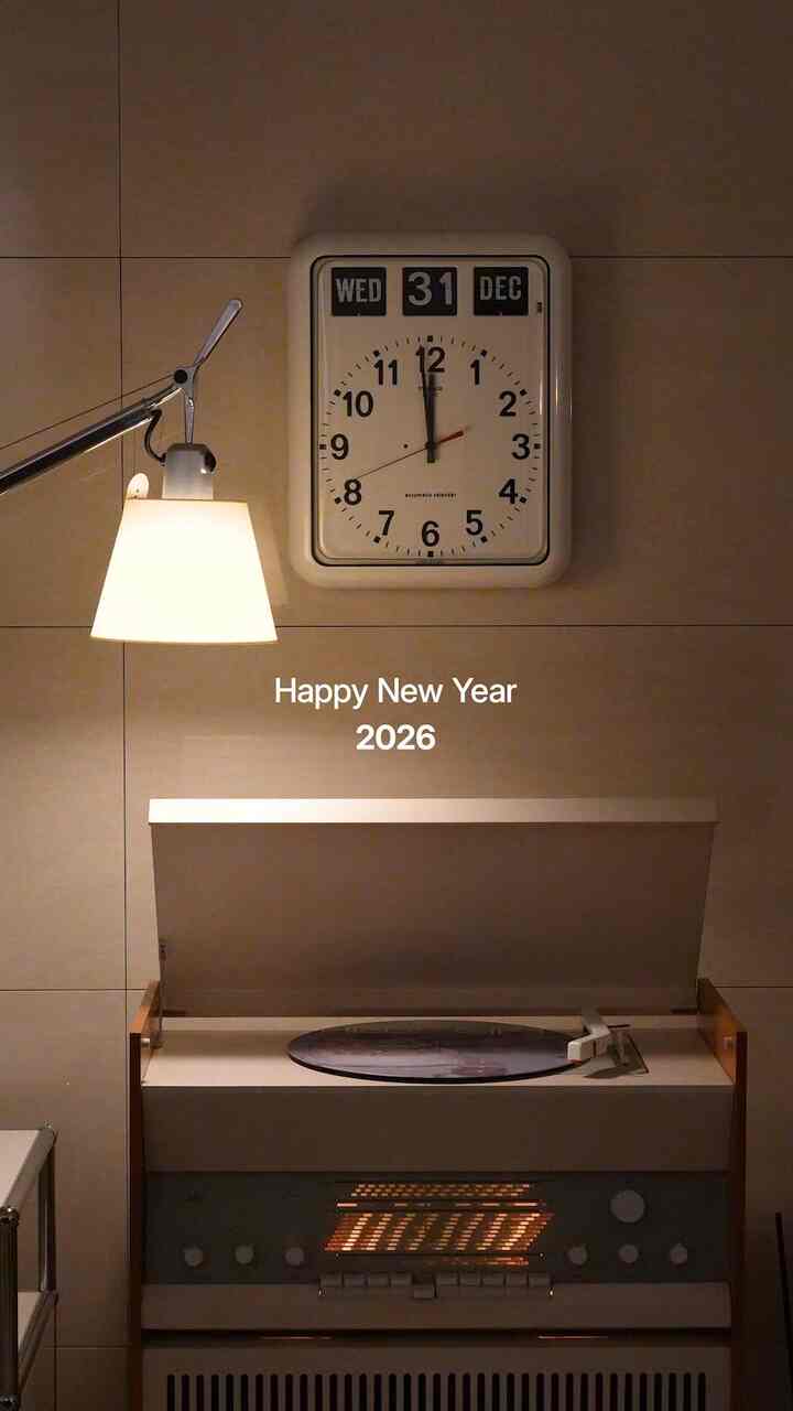 暖かいベージュ調のタイル壁に壁掛け時計、レトロなレコードプレーヤーとテーブルランプが配置された雰囲気のあるインテリア
