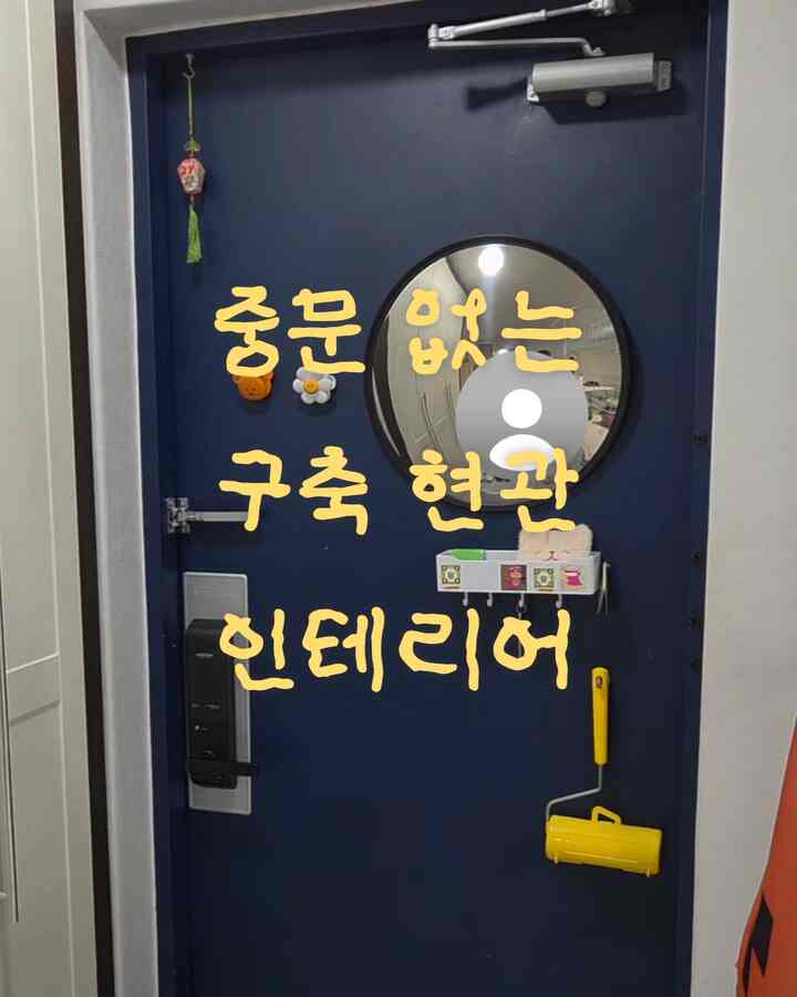 ネイビーのドアが中央にある間仕切りのない玄関、複数のマグネットと丸い鏡が配置された実用的な空間